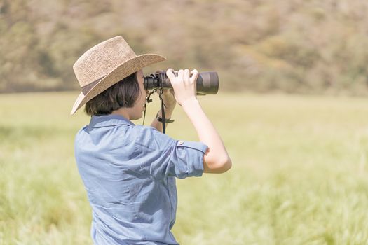 Young asian woman short hair wear hat and hold binocular in grass field countryside Thailand