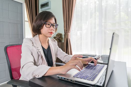 Young asian woman short hair in smart casual wear working on laptop while sitting near window in home office