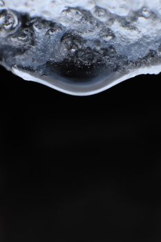 Handing down water drop from ice top. Cold clear rain drop with ice reflection inside. Macro closeup.
