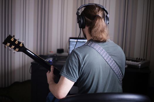 Bearded man musician playing music and composing a song with electric guitar piano and laptop computer while sitting in living room, corona virus quarantine stay home concept