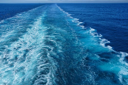 A Cruise ship wake on a beautiful sunny day with white clouds and blue seas on the Atlantic Ocean.