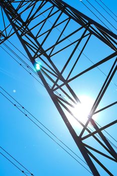 electricity pylons from low angle with blue sky and sun in background