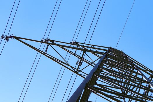 electricity pylons from low angle with blue sky and sun in background