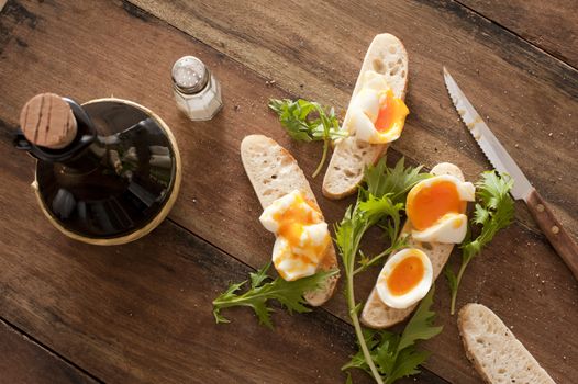 Snack of hard boiled eggs and fresh green herbs on baguette being prepared on a wooden kitchen table