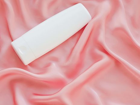 Blank label cosmetic container bottle as product mockup on pink silk background, hygiene and healthcare