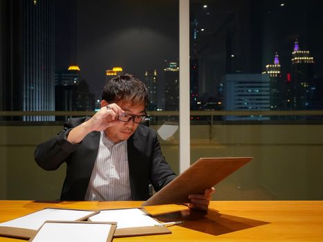 Asian businessman review brief document after work. Meeting room on high floor at the night time. Bangkok's bustling downtown area.