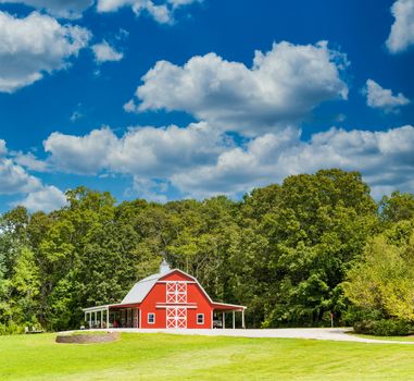 An old red, wooden barn on a green, grassy hill under nice skies