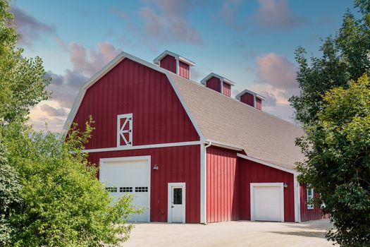 A traditional red barn near trees under blue skies