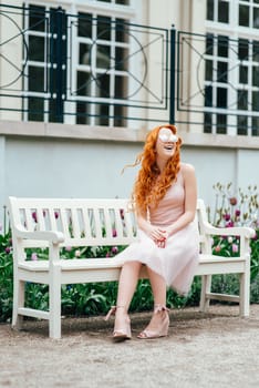 red-haired young girl walking in a park between trees and architectural objects