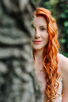 red-haired young girl walking in a park between trees and architectural objects