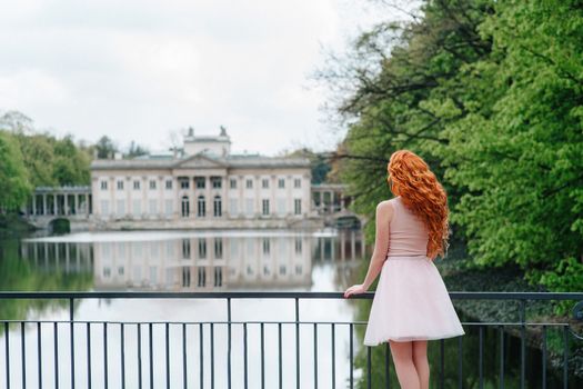 red-haired young girl walking in a park between trees and architectural objects