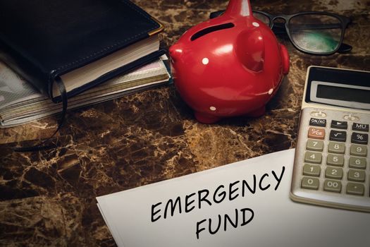 Emergency fund concept. The sheet with the text is next to the piggy Bank, diary and glasses