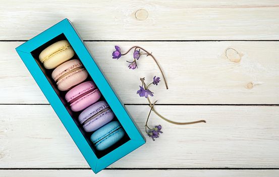 Macaroons in gift box next to violet on wooden background
