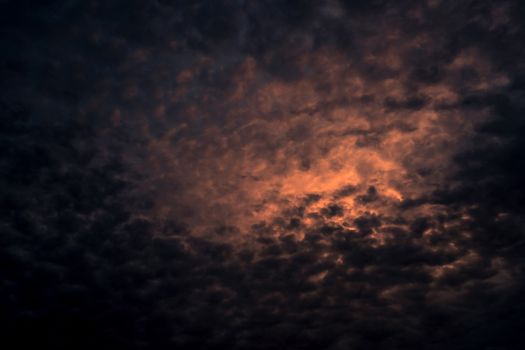 Red light of sun in dark cloudy sunset sky. Dramatic sky with beautiful pattern of fluffy clouds. Mental power or psychic power background. Power of nature. Exotic cloudscape. Climate change concept.