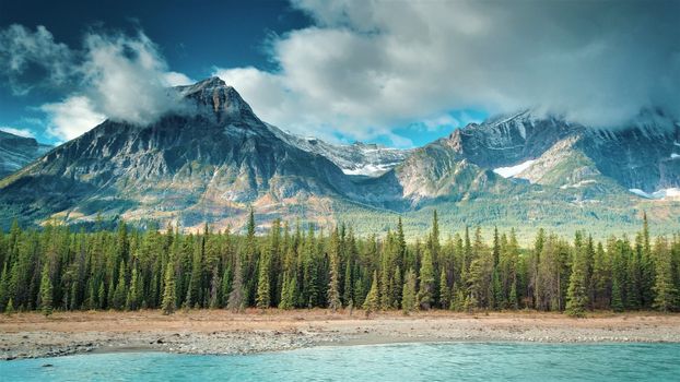 Aerial of Athabasca River in Jasper. River, Trees, sky clouds, mountain in image.