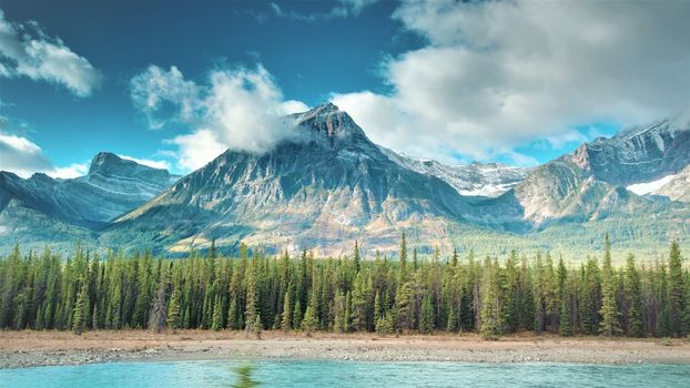 Aerial of Athabasca River in Jasper. River, Trees, sky clouds, mountain in image.