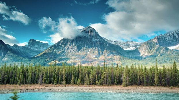 Aerial of Athabasca River in Jasper. River, Trees, sky clouds, mountain in image.