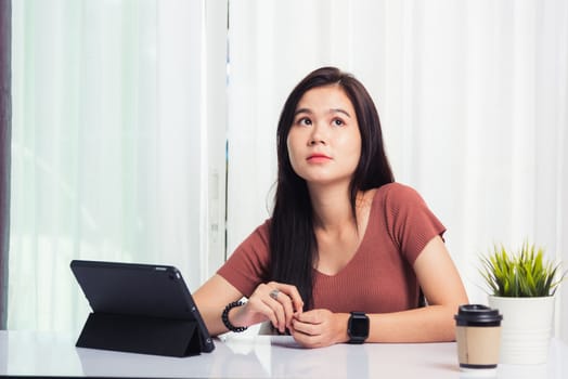 Work from home, Asian business young beautiful woman smiling sitting on desk workspace talking communicating with team video chat or conferencing on digital tablet computer at home office