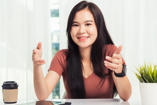 Work from home, Asian business young beautiful woman smiling sitting on desk workspace raise hand explain job communication with team video conferencing on digital tablet computer at home office