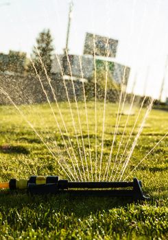 Lawn sprinkler spraying water over green grass. Modern device of irrigation garden grass. Irrigation system - technique of watering in the garden. Watering the Lawn with Sprinkler