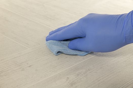 hand with blue rubber glove cleaning a floor with a wiping pad