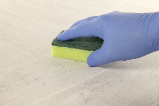 hand with blue rubber glove cleaning a floor with a green and yellow cleaning tool
