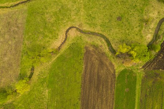 Green landscape from above: agriculture fields, pasture and small water stream