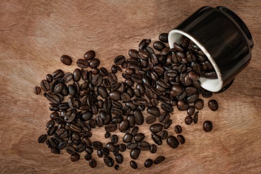 Cup of coffee lying on a wood from which roasted coffee beans come out