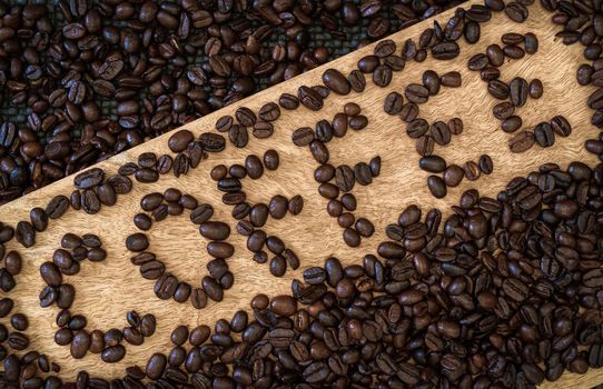 Roasted coffee beans on a wooden surface and the word cafe made with coffee beans