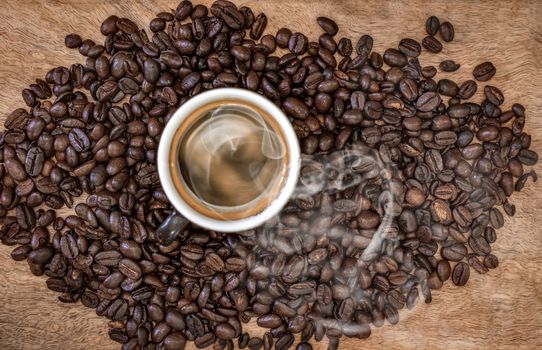 A group of roasted coffee beans with a cup of coffee in the middle with smoke coming out of it