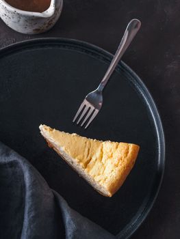 Plate with piece of cheesecake on dark background. Classic cheesecake, caramel sauce and dessert forks. Vertical. Top view or flat lay.