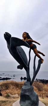 A girl statue with a turtle and seaweed as if swimming and looking at the blue sky in Jeju Island, South Korea