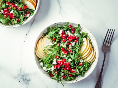 Vegan salad bowl with arugula, pear, pomegranate, coconut crumble or cottage cheese on marble tabletop. Vegan breakfast, vegetarian food, diet concept. Top view or flat lay.