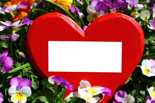 The picture shows a red wooden heart with a text space in pansies