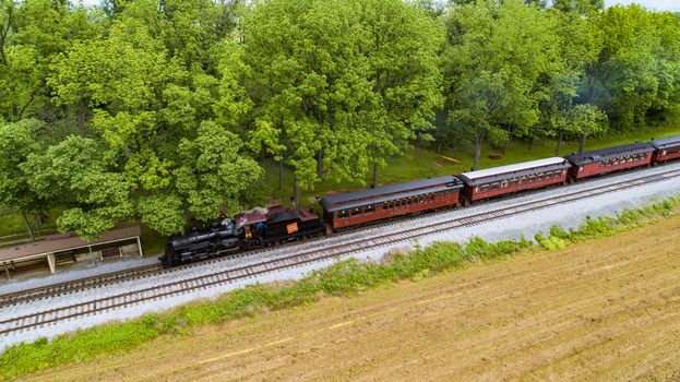 Ariel View of a Steam Passenger Train Pulling into Picnic Area Blowing Smoke on a Sunny Summer Day as seen by a Drone