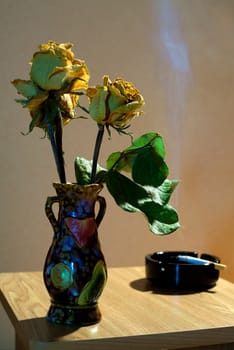 vase with yellow dried roses and ashtray with cigarette
