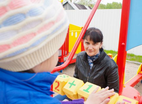 mother watching her daughter, counting on the dice on the playground on spring day