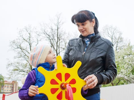 young mom plays with her daughter at the playground on a toy ship on spring day