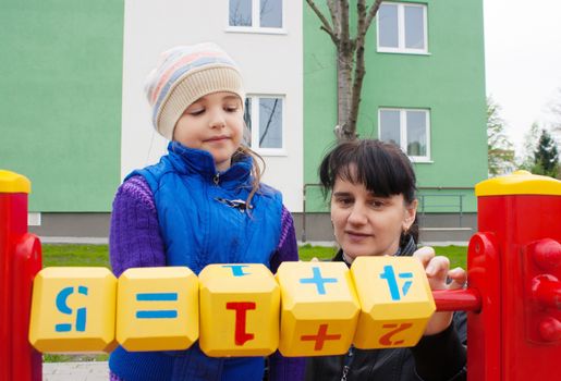 mom and daughter playing in the playground cubes with numbers on spring day