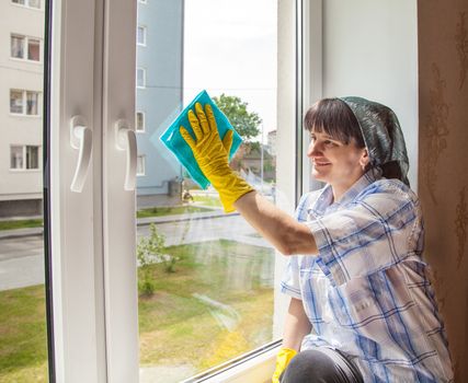 young smiling woman washes a window from the inside