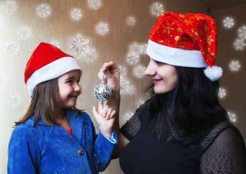 mother and daughter in Christmas caps holding mirror ball 