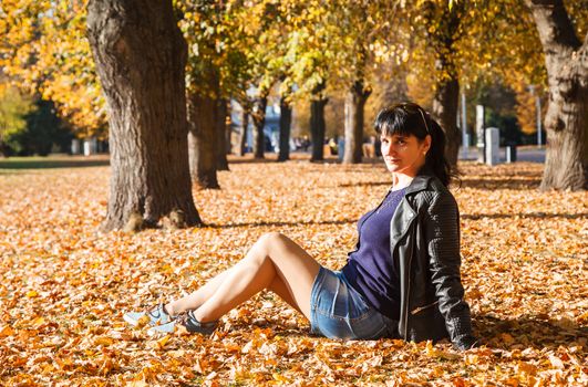 young brunette woman sitting on the grass in the park on sunny autumn day