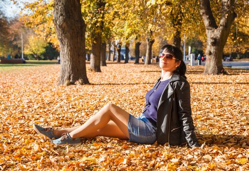 young brunette woman sitting on the grass in the park on sunny autumn day