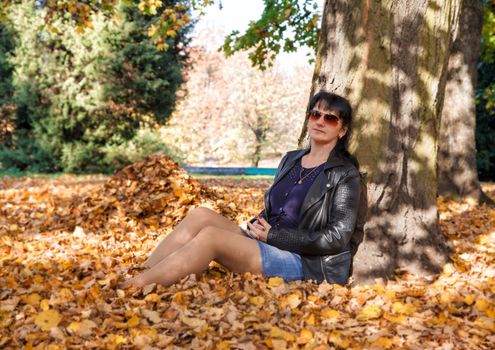 young brunette woman sitting on the grass in the park on sunny autumn day