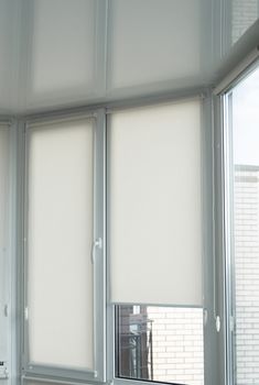 Details of white fabric roller blinds on the plastic window with wood texture in the living room