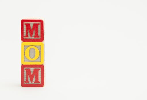 Three small wooden toy blocks spell the word mom in colorful letters on a white background.
