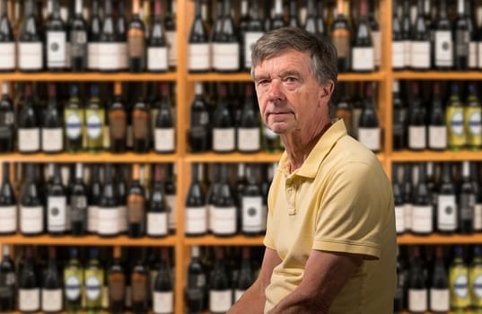 Senior old man looking at camera with a background of a wine cellar full of thousands of bottles on shelves