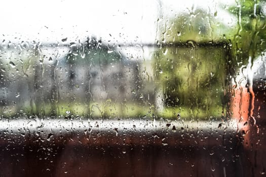 Raindrops on the window pane. Blurred background outside the window in the rain.