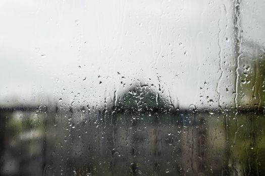 Raindrops on the window pane. Blurred background outside the window in the rain.
