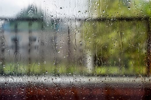 Raindrops on the window pane. Blurred background outside the window in the rain.